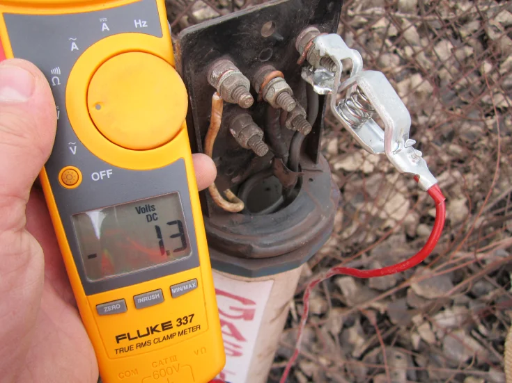 Technician measuring DC voltage at a cathodic protection test station with a clamp meter