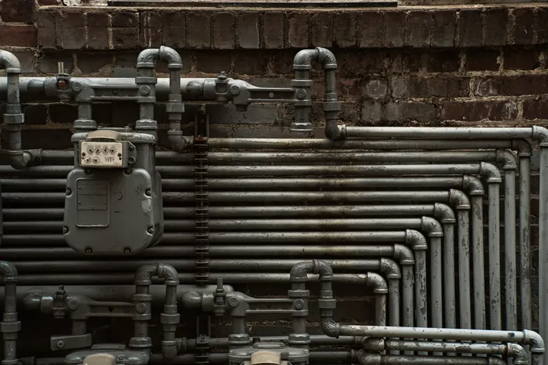 Close-up of steel piping and a gas meter on a brick wall