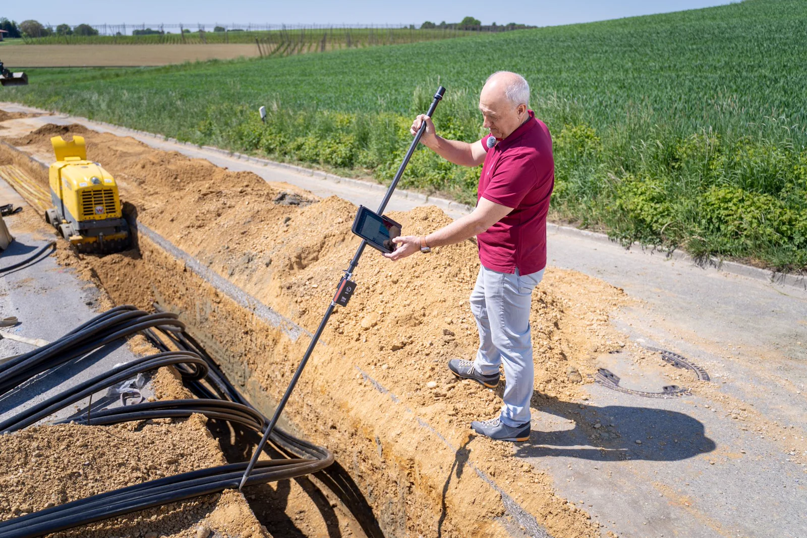 Technician performing a close-interval survey with a GNSS rover pole at an open pipeline trench