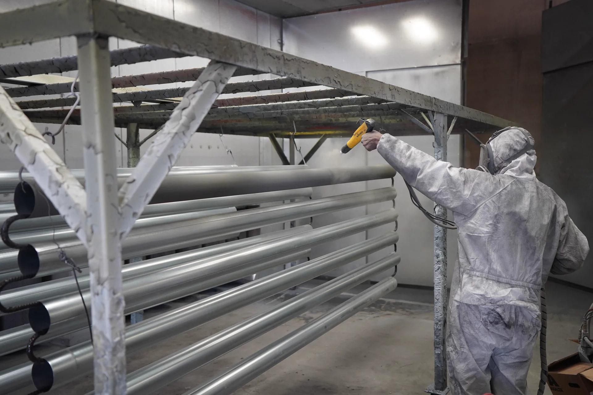 Technician applying powder coating to pipes on a production line, representative of a coating plant audit